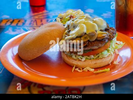 Hamburger sandwich with bun, mushrooms, cheese, lettuce and tomato on orange plate againist a blue background Stock Photo