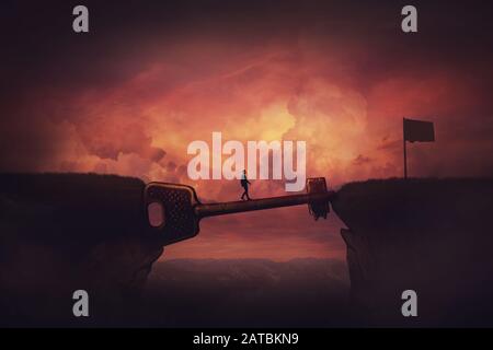 Conceptual view, businessman crosses a chasm obstacle balancing on a huge, golden key shaped bridge. Way to success concept, reach the finish flag. Ac Stock Photo