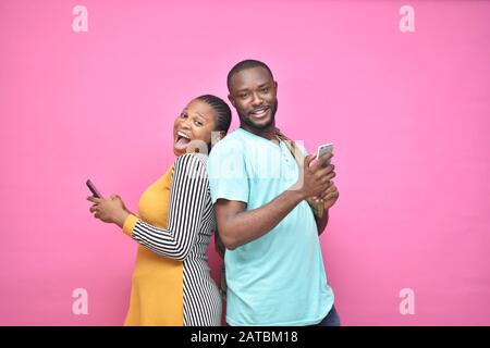 excited young black people standing back to back viewing contents on their phones, looking surprised, young african man and woman Stock Photo