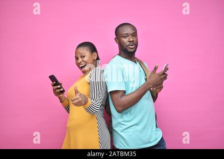 excited young black people standing back to back viewing contents on their phones, looking surprised, young african man and woman Stock Photo