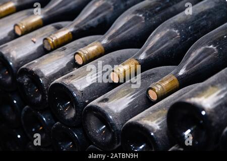 Ancient dark dusty wine bottles aging in underground cellar in rows. Concept winery vault with rare wines, exclusive collection. Stacks of wine bottle Stock Photo