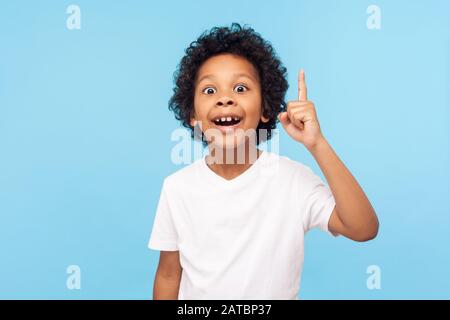 Eureka! Portrait of smart little boy with curly hair pointing finger up and looking inspired by genius thought, showing good idea sign, having clever Stock Photo