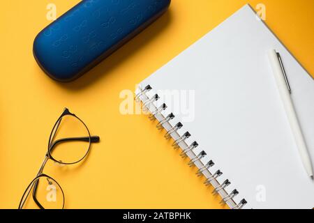 Stock photo of a blank open notebook page, glasses and a blue case on a yellow background Stock Photo