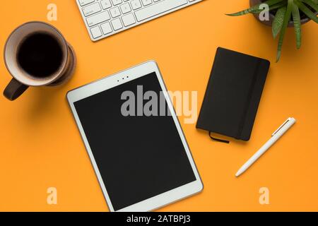 Stock photo of a white tablet with a black notebook, a white pen and some desktop objects on a yellow background Stock Photo