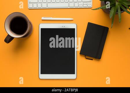 Stock photo of a white tablet with a black notebook, a white pen and some desktop objects on a yellow background Stock Photo