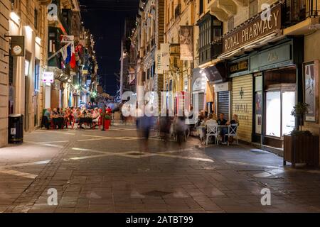 Valletta, Malta - October 14, 2019: People stroll and enjoy their meals at the Republic Street at night, main pedestrian street in the capital city Stock Photo