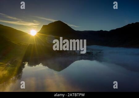 Dawn mist rises around Buttermere, the lake in the English Lake District in North West England. The adjacent village of Buttermere takes its name from Stock Photo