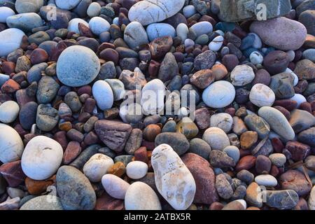 Pebbles on the beach, peaceful background of white, gray and red rocks. Close up of various small stones, round shape, bright light Stock Photo