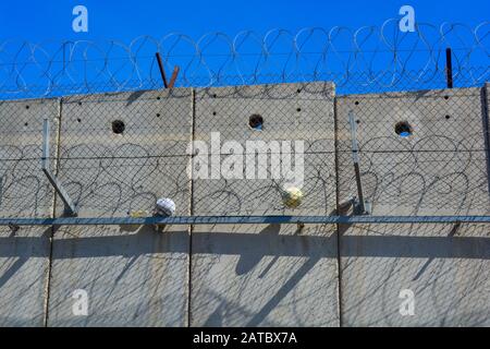 A closeup of the separation wall between Israel and Palestine. Two balls from kids in the West Bank caught in the barbed wire and fence. A symbol of d Stock Photo