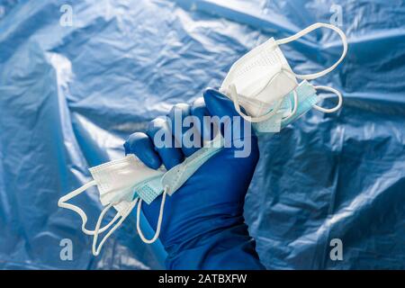A hand in blue medical glove holding a bunch of face masks on blurry plastic film background. Symbol of coronavirus pandemic resistance and help. Stock Photo