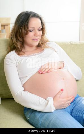 Happy pregnant woman sitting on the couch at home. The ninth month of pregnancy. Stock Photo