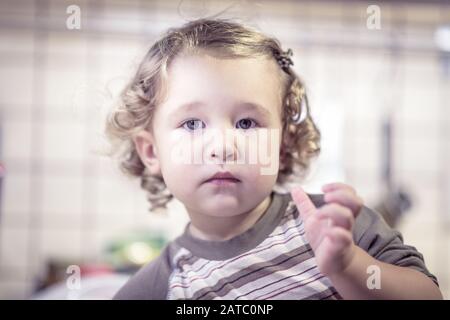Cute two-year-old girl washes the dishes in kitchen. Little child is posing for a photo. Stock Photo