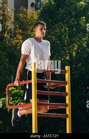 Young attractive caucasian crossfit sportsman working out in park, exercising on chin-up bar, doing dips for arms and back muscles Stock Photo