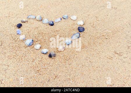 Heart built of sea shells on the sand. Romantic symbol of love made on a beach in summer. Small seashells lie in the shape of the heart for background Stock Photo