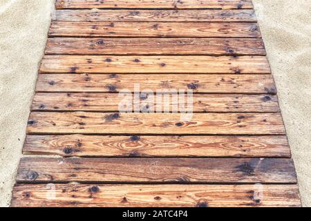Wooden pathway on a sandy beach in summer. Natural wood planks background. The tourist track with an old decking to sea close-up. Top view of footpath Stock Photo