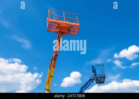 Cherry pickers on blue sky background. Boom with lift buckets of heavy machinery. Platforms of the telescopic construction lifts in summer. Stock Photo