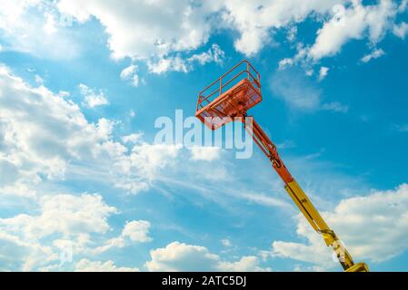 Cherry picker on the blue sky background. Boom with lift bucket of heavy machinery. View of the platform of the telescopic construction lift in summer Stock Photo