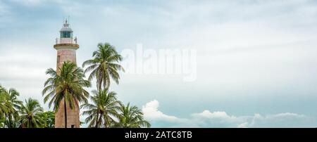 Lighthouse and palm trees on the sky background. Scenic panoramic view of old lighthouse on tropical coast in summer. Beautiful landscape with copy sp Stock Photo