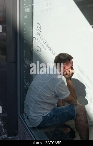 Photo shot through a shop window of a man with his chin in his hand looking bored Stock Photo