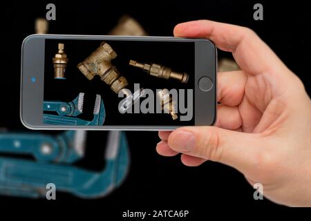 Plumbing tools on black background. Faucets, valve, pipe wrench to repair water supply system. Plumber tools on smartphone screen. Stock Photo