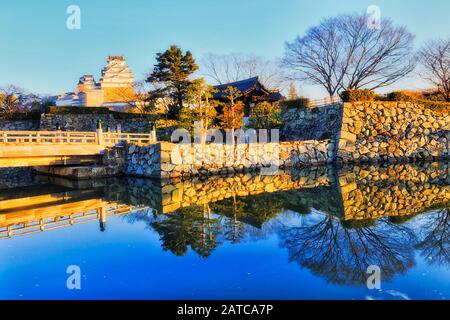 Wooden bridge over water-filled moat around white castle near Osaka in Japan – Himeji-jo on a sunny morning. Stock Photo