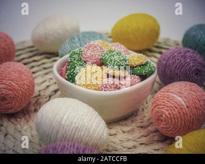Decorated colorful Easter eggs on a placemat with a small white bowl full of white chocolate colored mint candies with white dots all over them. Stock Photo
