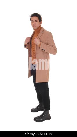 A tall young man standing in a beige coat in profile in the studio looking at the camera, isolated for white background Stock Photo