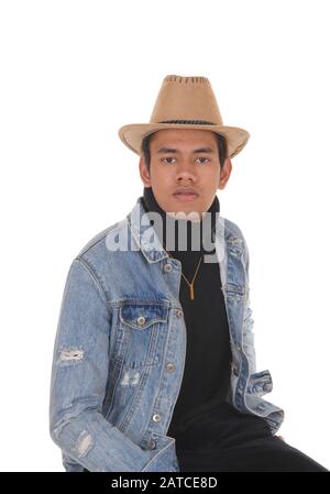 A handsome young man siting on a chair with a jeans jacket and  cowboy hat and black pants, isolated for white background Stock Photo
