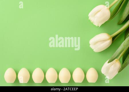 Easter still life. White chocolate eggs and tulips on green background. Copy space. Stock Photo