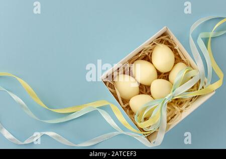 Easter still life. The white chocolate eggs in the box are decorated with colored ribbon. Copy space. Stock Photo