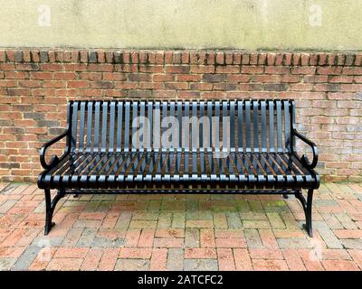 an empty black garden path bench next to a brick wall Stock Photo