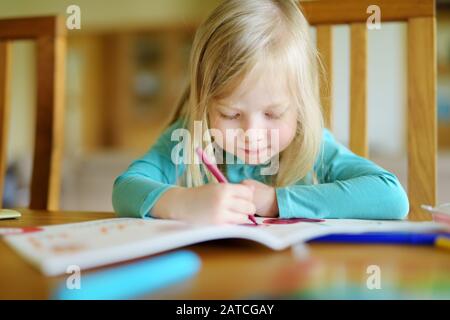 Cute little girl drawing with colorful pencils at a daycare. Creative kid painting at school. Girl doing homework at home. Stock Photo