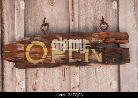 Wooden signboard open with rope hanging on planks background. Old wooden hanging on the wooden door open with a text Stock Photo