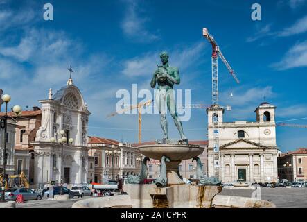 Statue at fountain, churches under repairs after 2009 earthquake, 2018 view, Piazza Duomo, L'Aquila, Abruzzo, Italy Stock Photo
