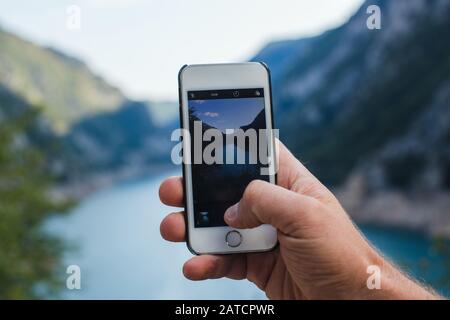 A man takes a picture of mountain landscape on the phone while holding it in one hand Stock Photo