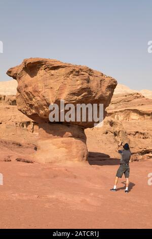 Traveler, senior man, taking a photo of red sandstone hoodoo rock called the Mushroom while hiking in the Negev desert, Timna Park, Israel Stock Photo