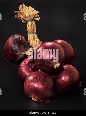 Close-up of a bunch of red Tropea onions tied on a black background Stock Photo