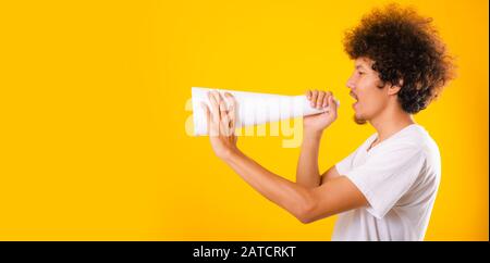 Asian handsome man with curly hair he announcing or spreading news using white speaker paper isolate on yellow background Stock Photo