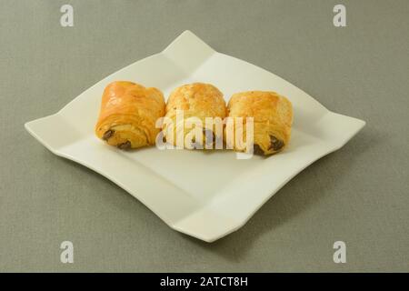 Three breakfast chocolate mini croissant pastries on white plate on grey tablecloth Stock Photo