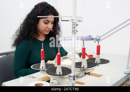 Young woman using professional overlock sewing machine in workshop. Equipment for edging, hemming or seaming clothes at tailors shop Stock Photo