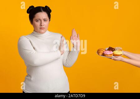 Fatty girl refusing consume tasty delicious sweets on plate Stock Photo