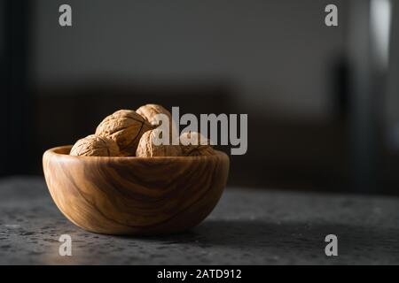 inshell walnuts in olive wood bowl on terrazzo countertop, shallow focus Stock Photo