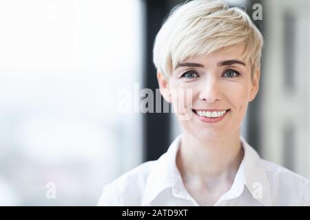 Mature Woman Smiling Standing Against Window Indoors, Portrait Stock Photo