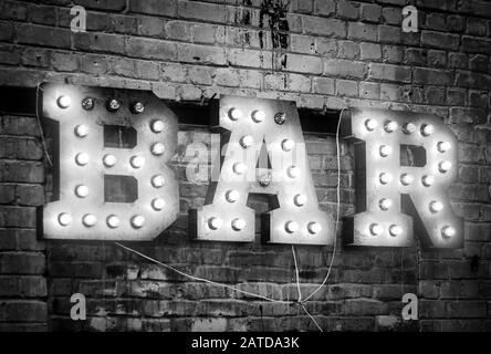 Bar signboard. Inscription from large metal letters decorated with glowing light bulbs on the brick wall Stock Photo