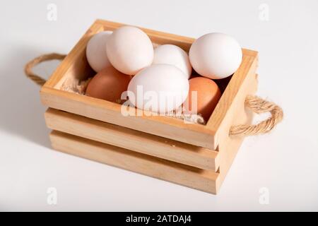 Close-up duck eggs and chicken eggs are put in a wooden basket placed on a white table. Stock Photo