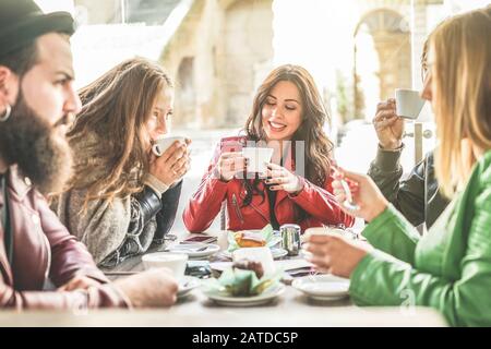Young friends toasting coffee and doing breakfast in bar bakery shop - Happy hipster people drinking cappuccino and eating muffins - Friendship concep Stock Photo