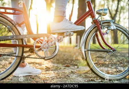 Young woman on old style italian bicycle with back light - Close up of girl feet riding vintage bike in park outdoor for fall time - Vintage fashion c