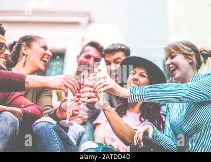 Happy friends cheering with champagne and making party outdoor - Loud fest, fun and drunk concept - Main focus on left man hand - Radial purple and bl Stock Photo