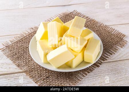 Rectangular pieces of fresh yellow butter on a white saucer over a white wooden table. Dairy. Sandwich butter. Natural fat nutrient. Front view. Stock Photo