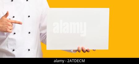 Unrecognizable Chef Showing Blank Poster Over Yellow Background, Panorama, Cropped Stock Photo
